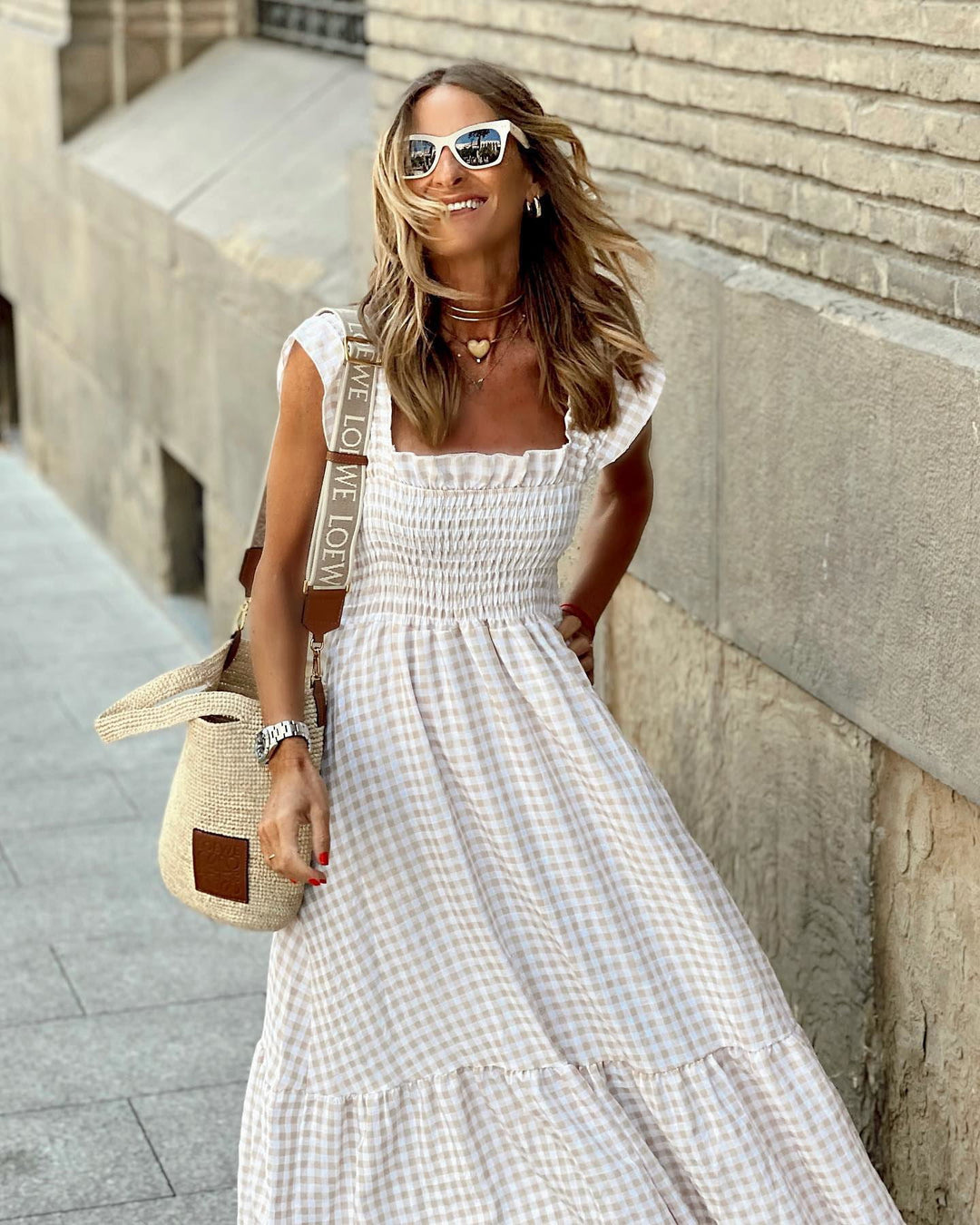 Woman in a white checkered dress standing against a stone wall.