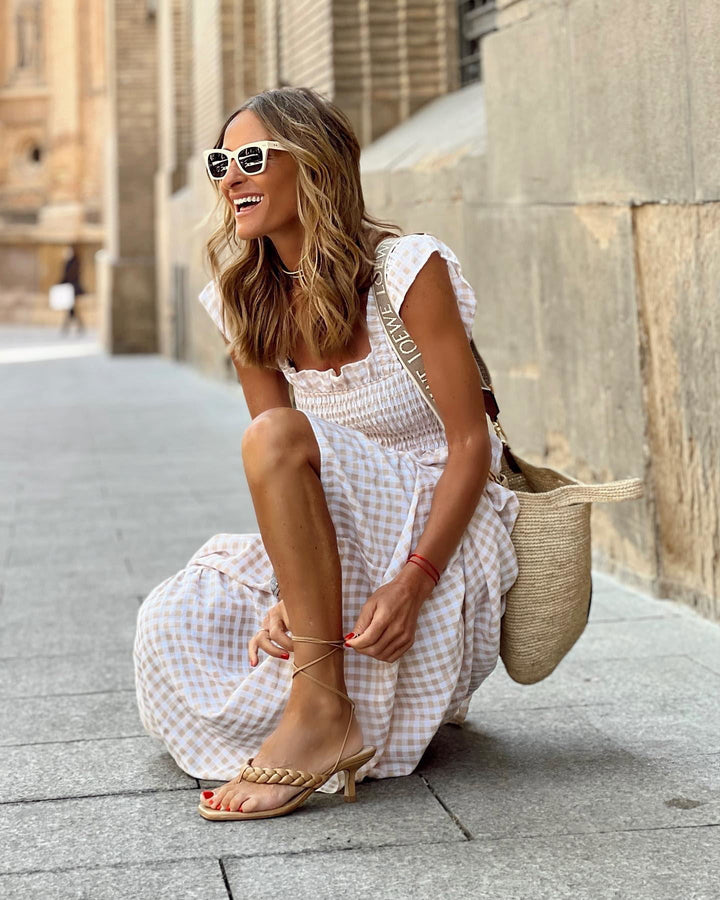 Woman in a white dress sitting on a stone pavement with a straw bag.