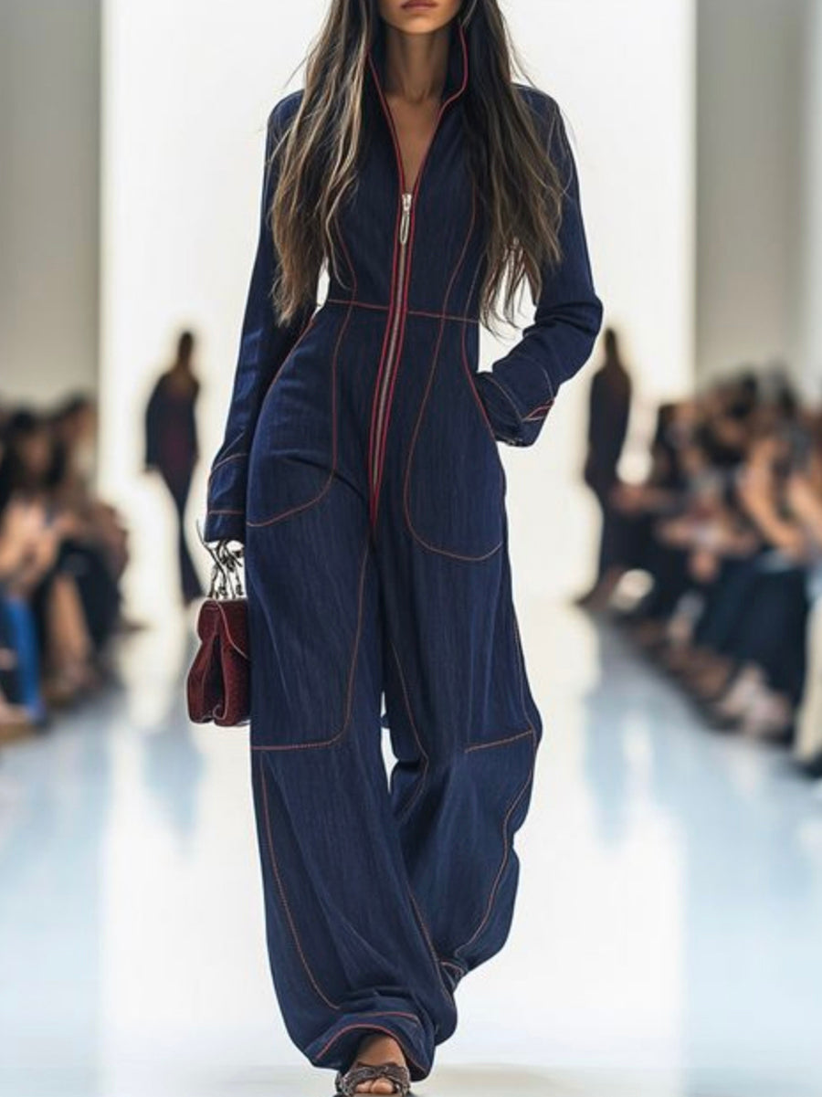 Model wearing a blue jumpsuit on a runway with blurred audience in the background