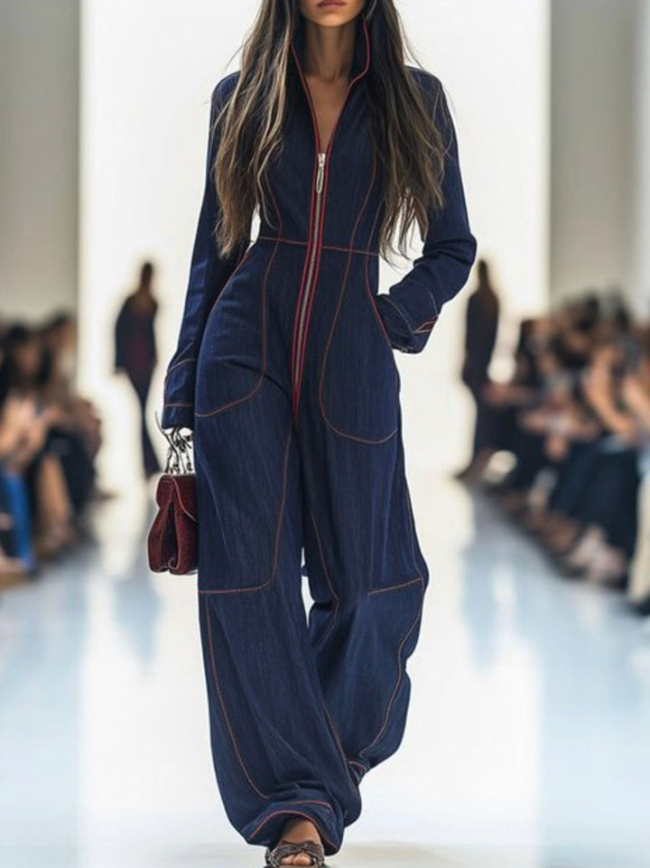Model wearing a blue jumpsuit on a runway with blurred audience in the background