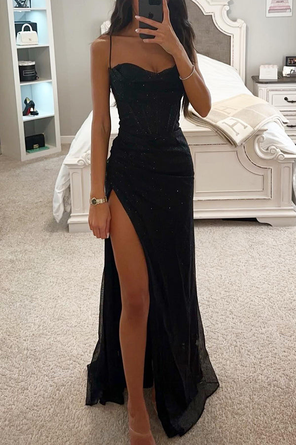 Person wearing a black strapless dress with a high slit in a bedroom setting.