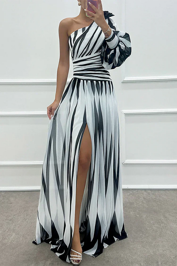 Woman wearing a black and white striped dress with a high slit, standing against a white wall.