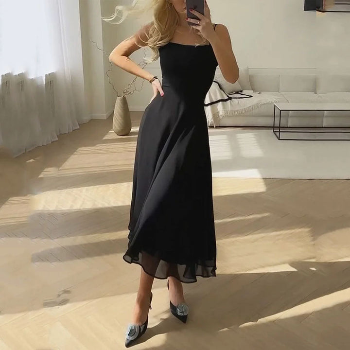 Woman in a black dress taking a mirror selfie in a modern living room.