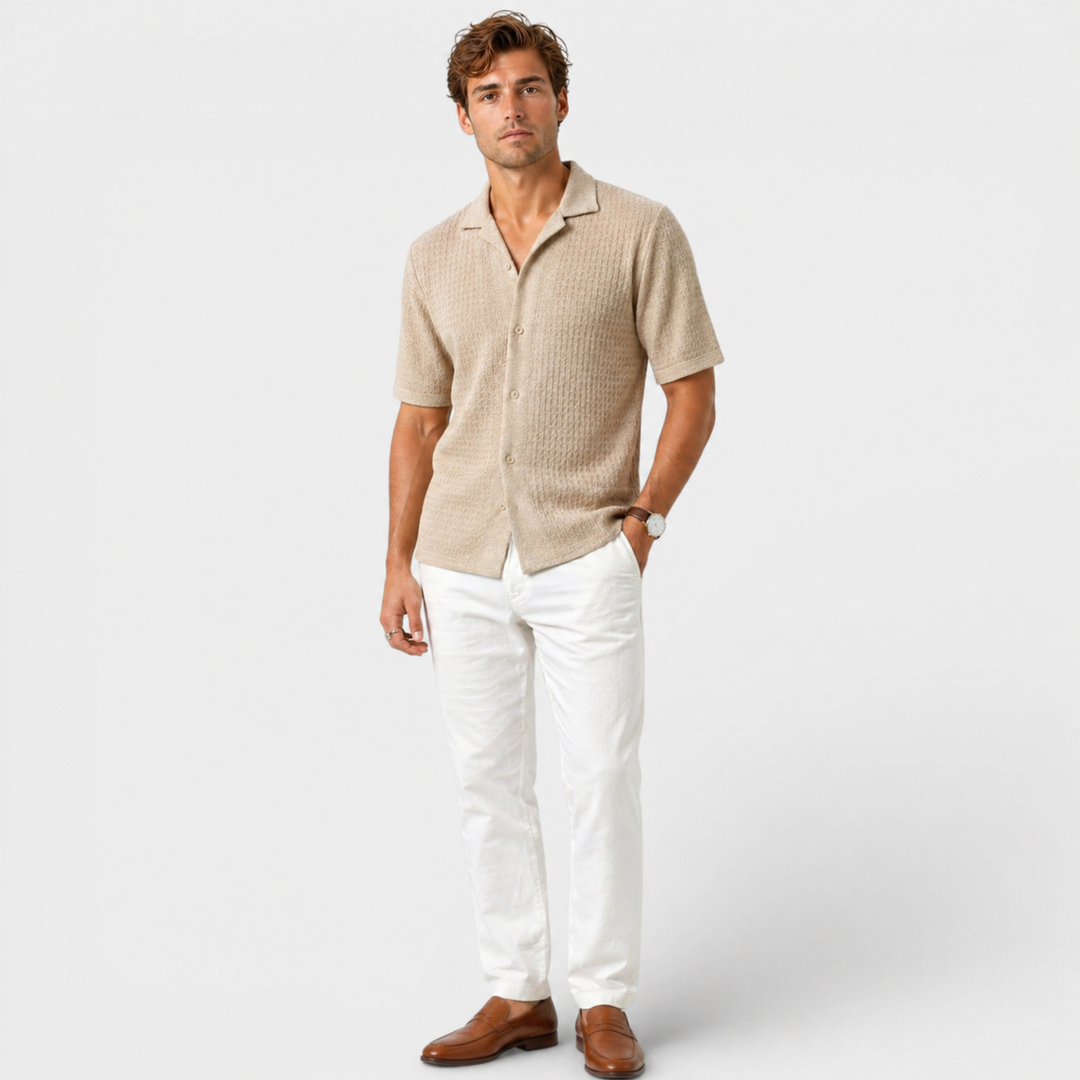 Man wearing a beige short-sleeve shirt and white pants on a light gray background