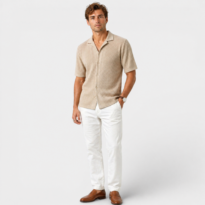 Man wearing a beige short-sleeve shirt and white pants on a light gray background