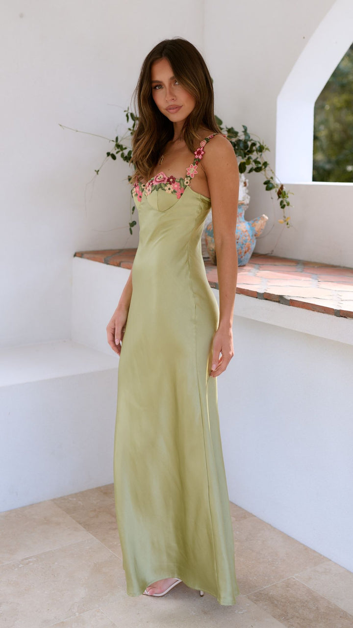 Woman wearing a light green dress with floral details in an outdoor setting.