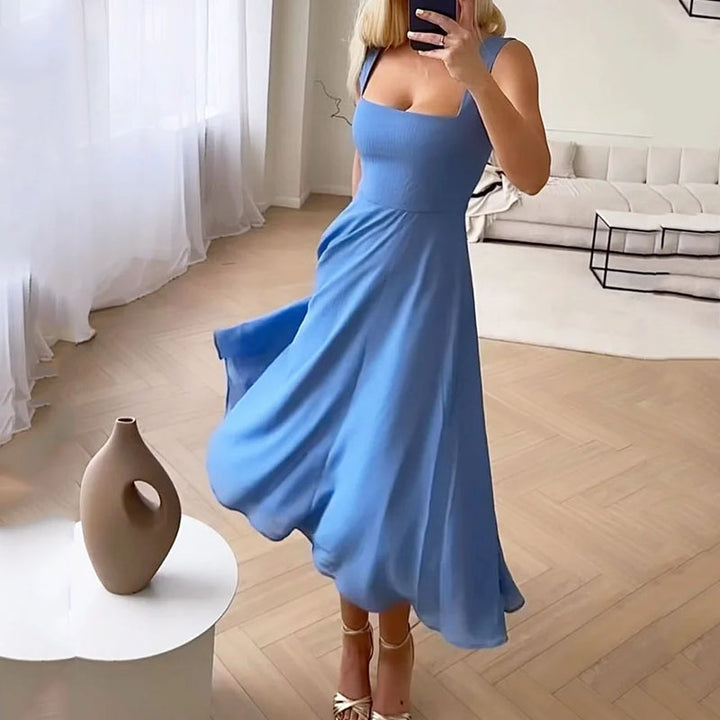 Woman in a blue dress taking a mirror selfie in a room with a vase on a table.