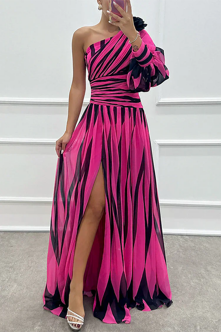 Woman wearing a pink and black striped one-shoulder dress with a slit, standing against a white wall.
