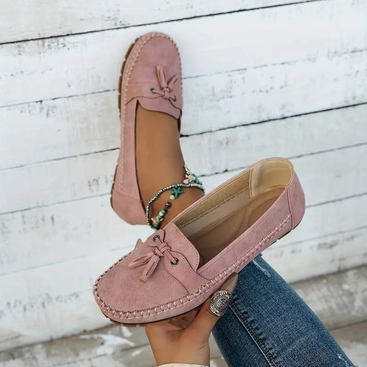Pink loafers worn with jeans on a wooden floor background