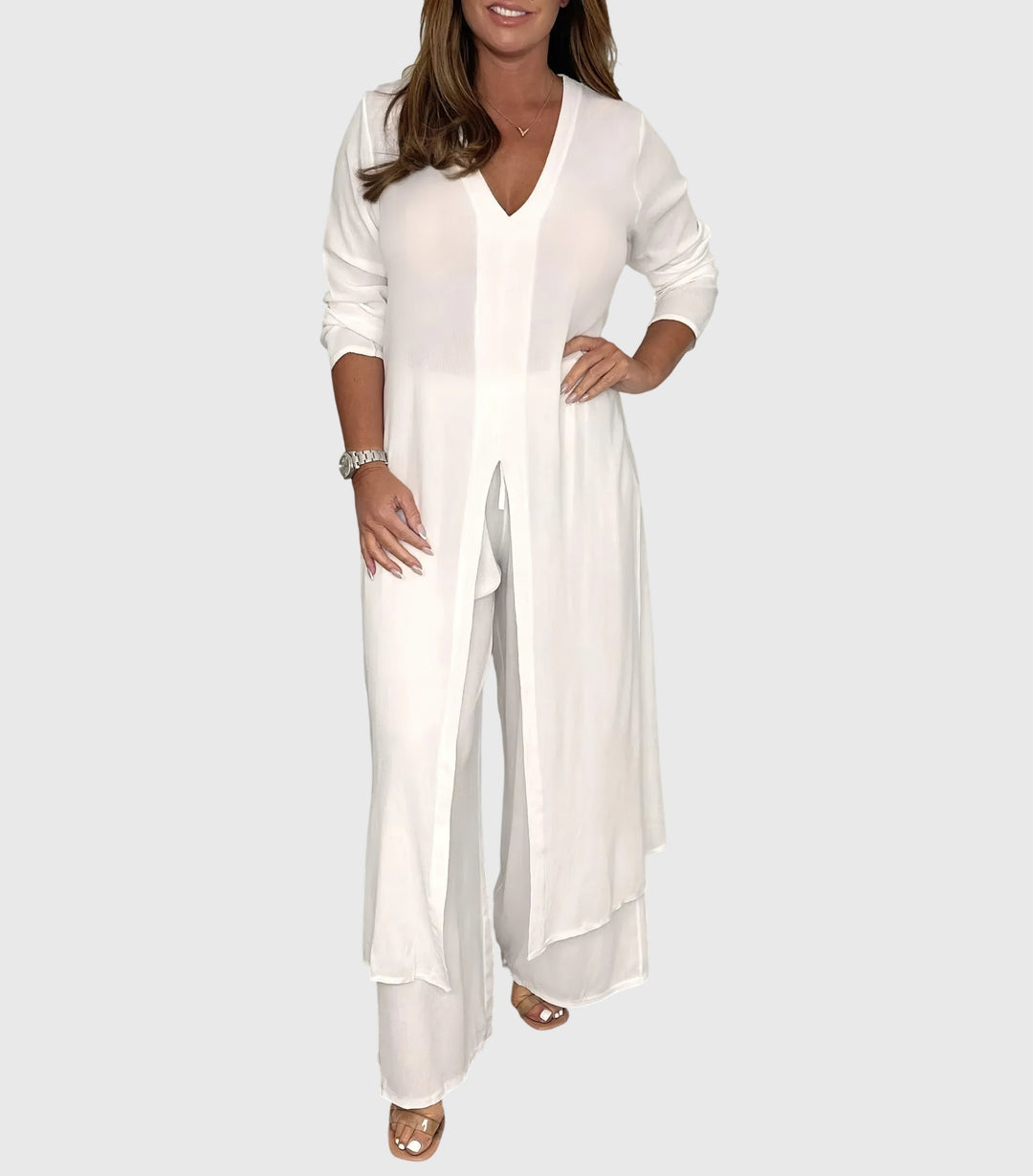 Woman wearing a white outfit with a long top and wide-leg pants on a plain background