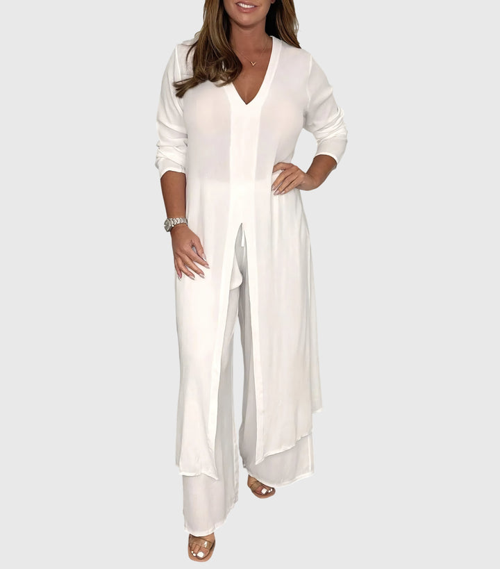 Woman wearing a white outfit with a long top and wide-leg pants on a plain background