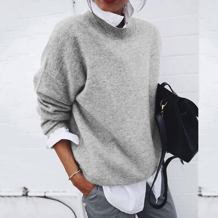 Person wearing a gray sweater over a white shirt with a black backpack against a white background