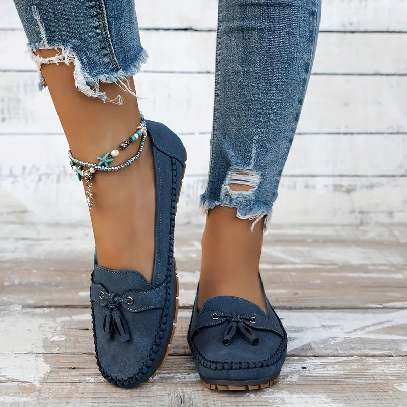 Navy blue loafers worn with ripped jeans on a wooden floor.