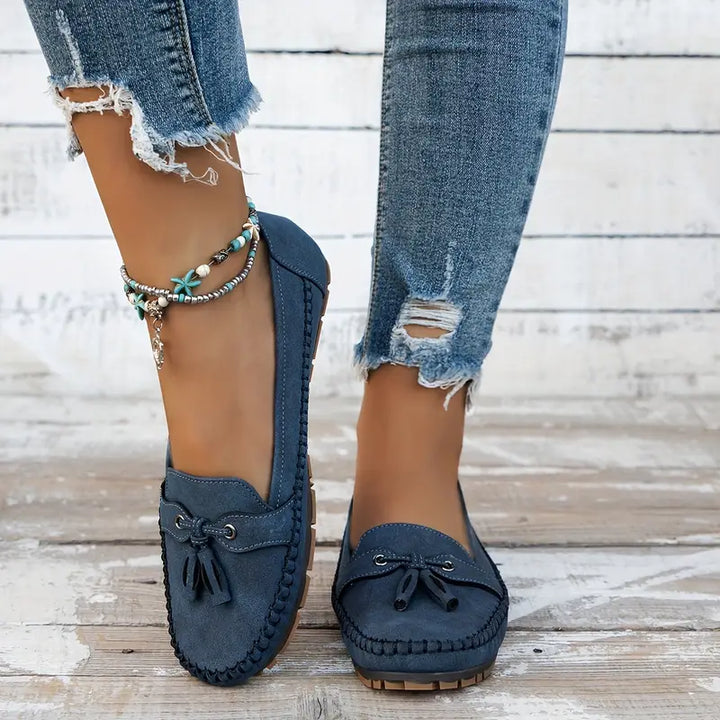 Navy blue loafers worn with ripped jeans on a wooden floor.