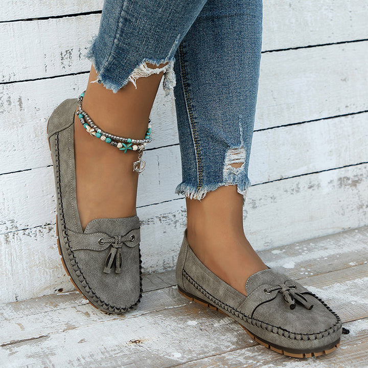 Gray suede loafers worn with ripped jeans on a wooden floor.