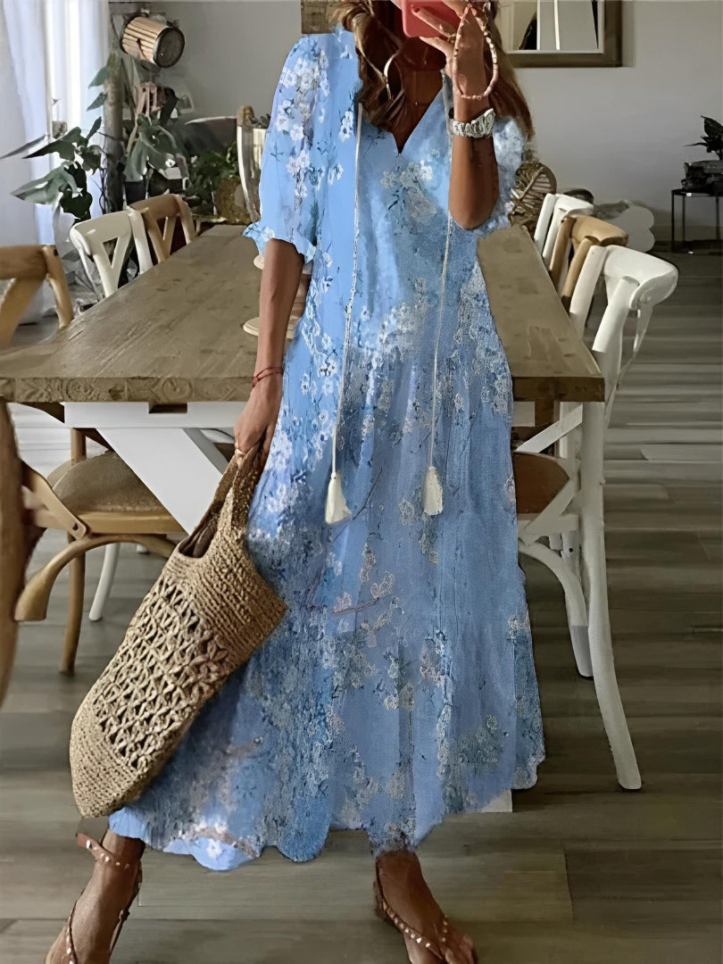 Woman in a blue floral dress holding a woven bag in a dining room.