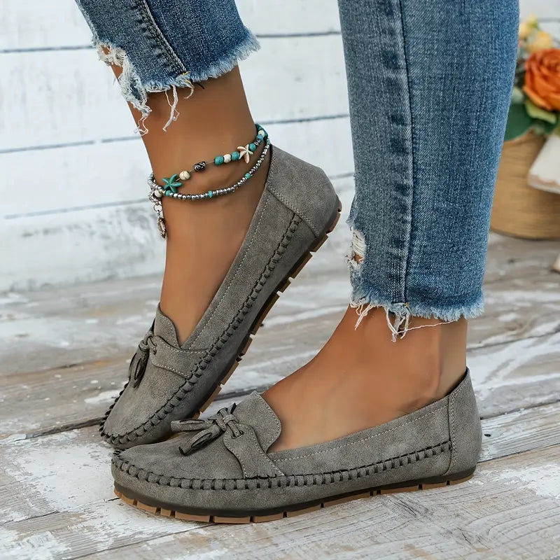 Gray loafers worn with ripped jeans on a wooden floor.