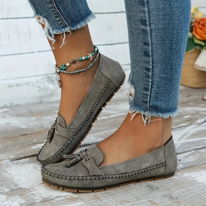 Gray loafers worn with ripped jeans on a wooden floor.