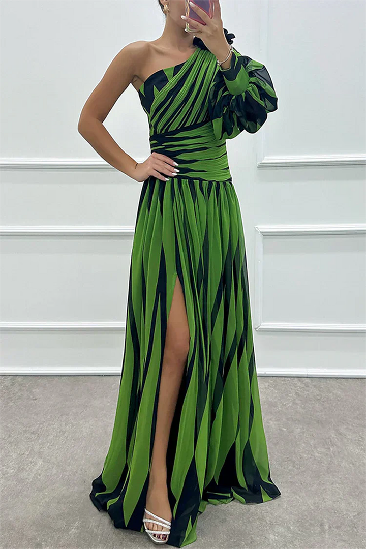 Woman wearing a green and black striped dress with a slit, standing against a white wall.