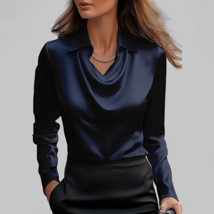 Woman wearing a navy blue long-sleeve top with a draped neckline on a gray background