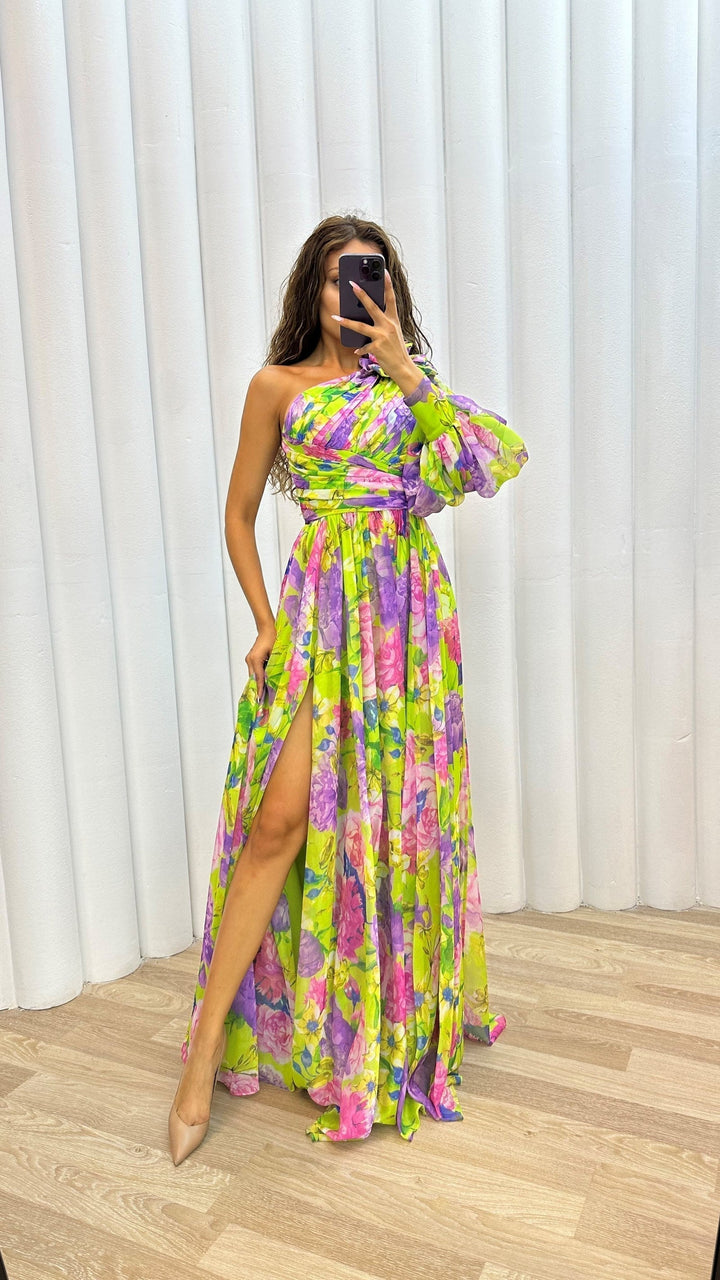 Woman wearing a colorful floral dress with a high slit in front of white curtains.