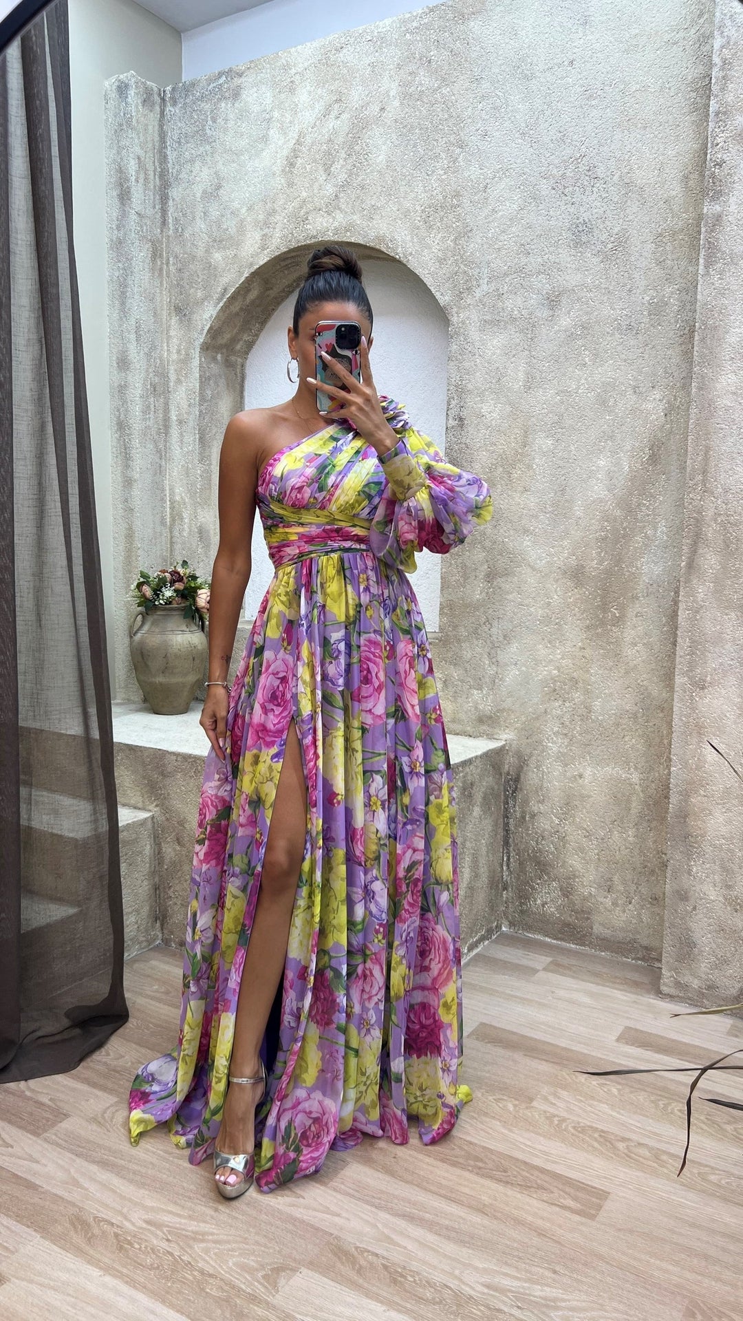 Woman in a colorful floral dress taking a mirror selfie in an outdoor setting.