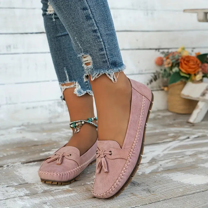 Pink loafers worn with ripped jeans on a wooden floor.