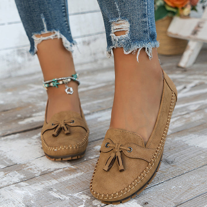 Brown suede loafers worn with ripped jeans on a wooden floor.