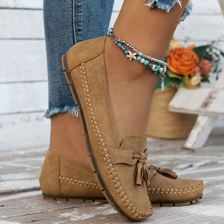 Brown suede moccasins worn with denim jeans on a wooden floor.