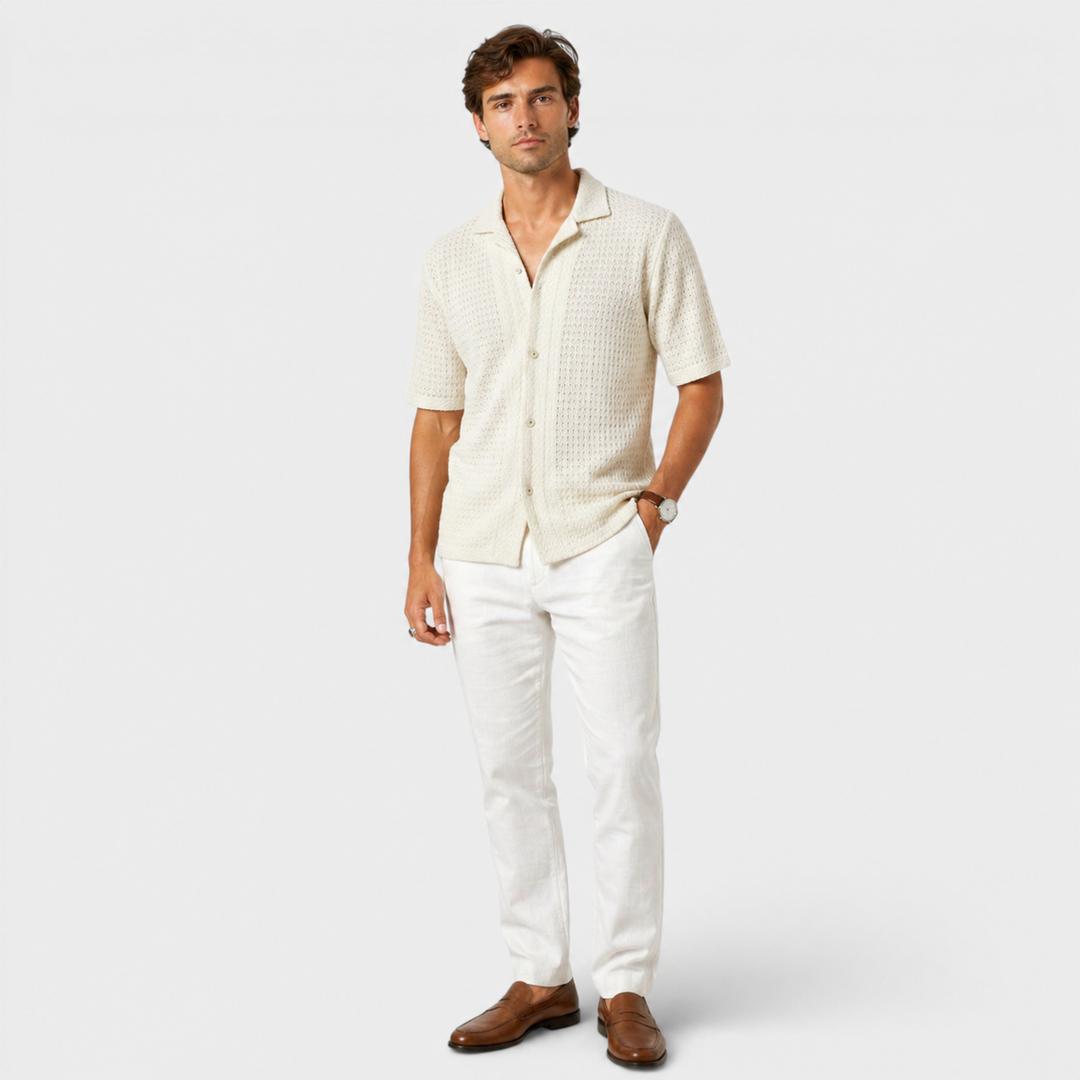 Man wearing a beige patterned shirt and white pants on a light gray background