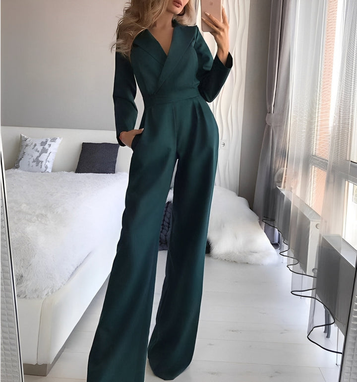 Woman taking a mirror selfie wearing a dark green jumpsuit in a bedroom.