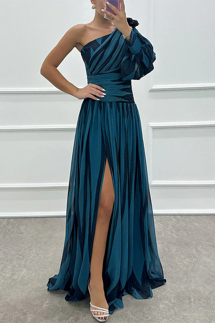 Woman wearing a teal one-shoulder dress with a slit, standing against a white wall.