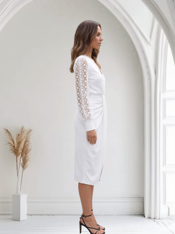 Woman wearing a white dress with lace sleeves in a bright, minimalistic room.