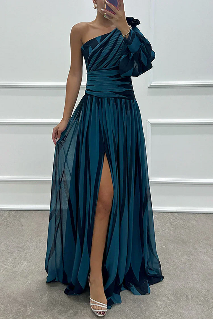 Woman wearing a teal one-shoulder dress with a slit, standing against a white wall.