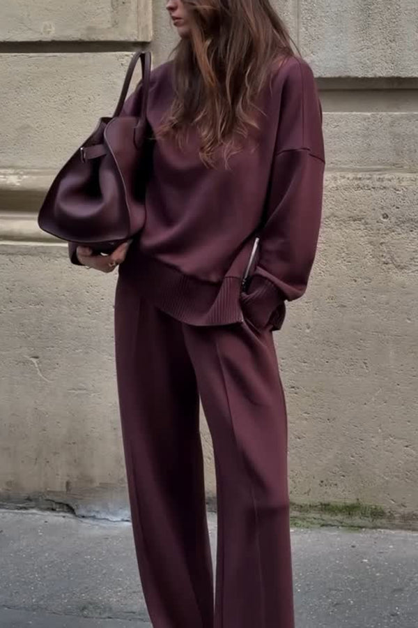 Person wearing a burgundy outfit with a matching handbag against a beige wall.