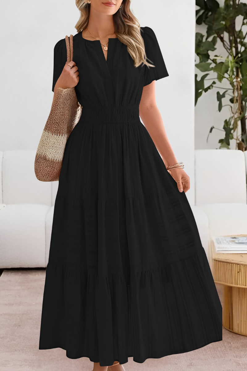 Woman wearing a black dress holding a patterned handbag indoors.