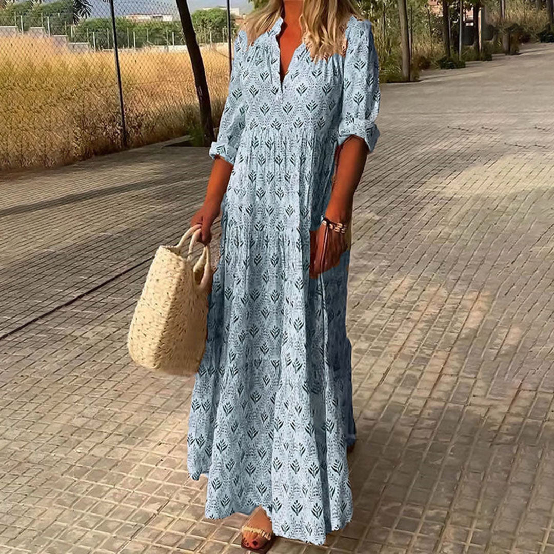 Woman in a long blue patterned dress walking on a paved path.