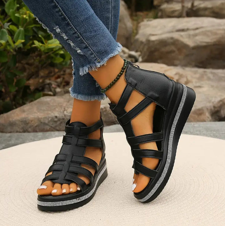 Black strappy sandals worn with ripped jeans on a natural background