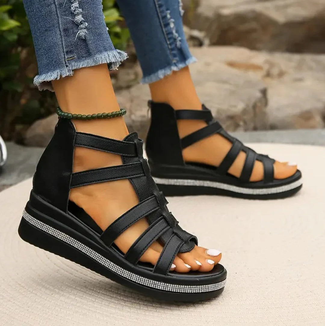 Black strappy sandals worn with ripped jeans on a blurred natural background