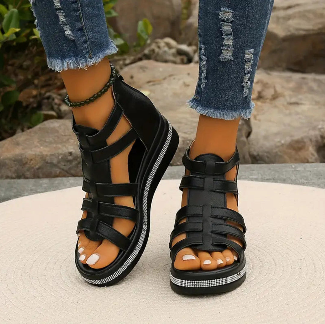 Black strappy sandals worn with ripped jeans on a neutral background