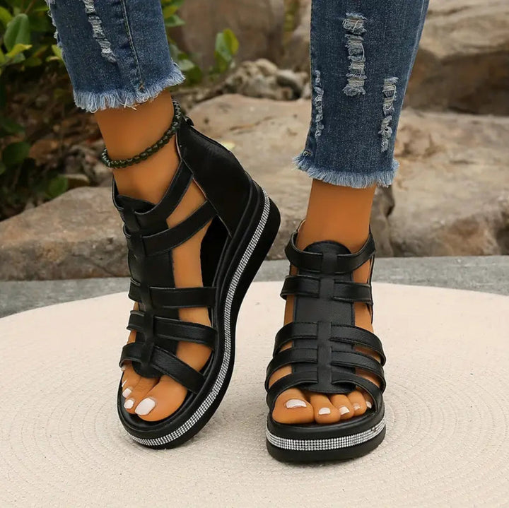 Black strappy sandals worn with ripped jeans on a neutral background