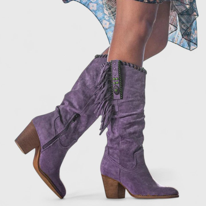 Purple suede boots with fringe details on a white background
