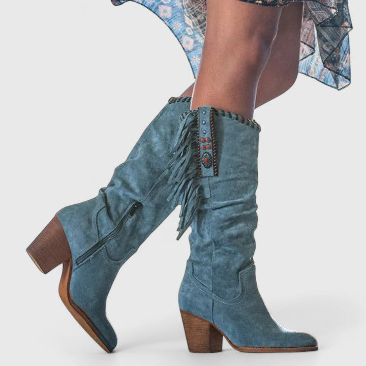 Blue suede knee-high boots with fringe details on a white background