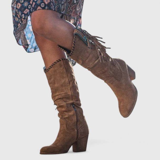 Brown suede knee-high boots with fringe details on a light gray background