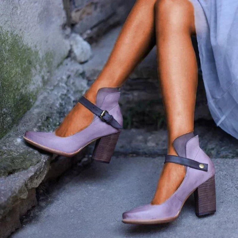 Purple high-heeled shoes with brown soles worn by a person sitting on a stone step.
