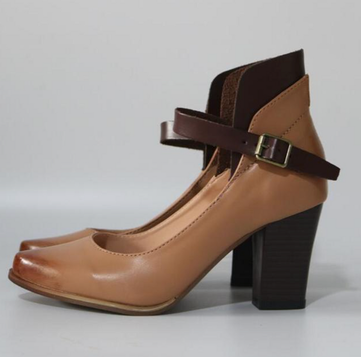 Tan high-heeled shoe with brown strap and buckle on a gray background
