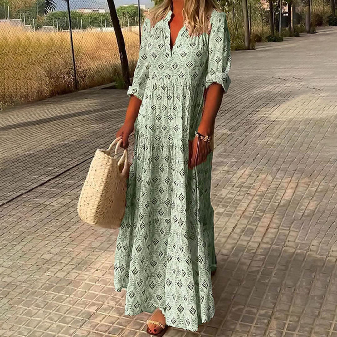 Woman in a long green dress walking on a paved path with a straw bag.