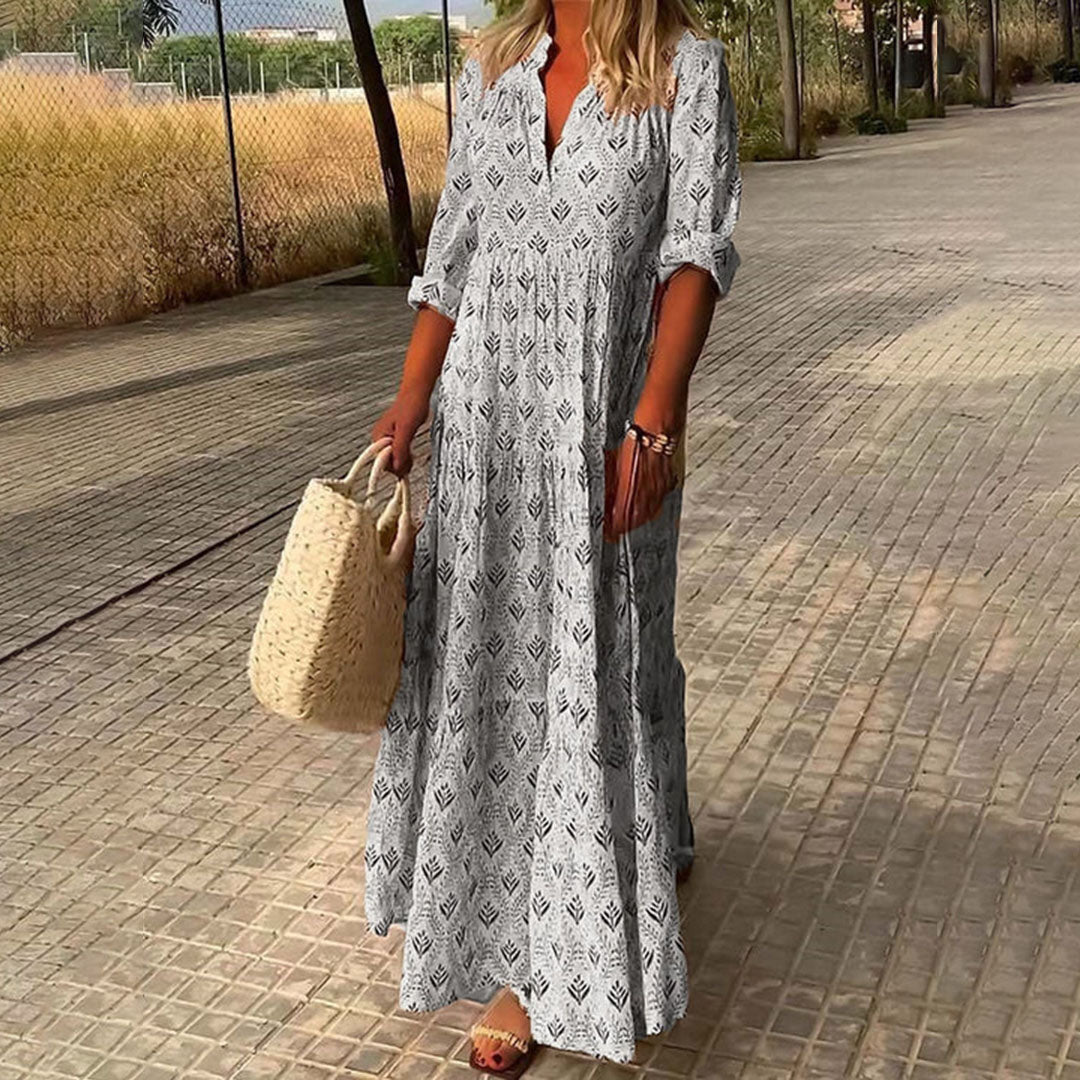 Woman in a long patterned dress holding a straw bag on a paved walkway.