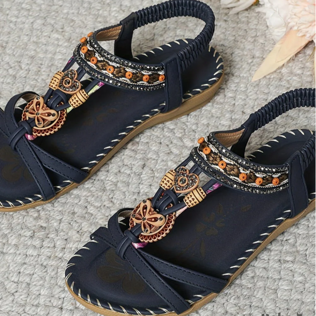 Navy sandals with decorative straps and embellishments on a textured surface