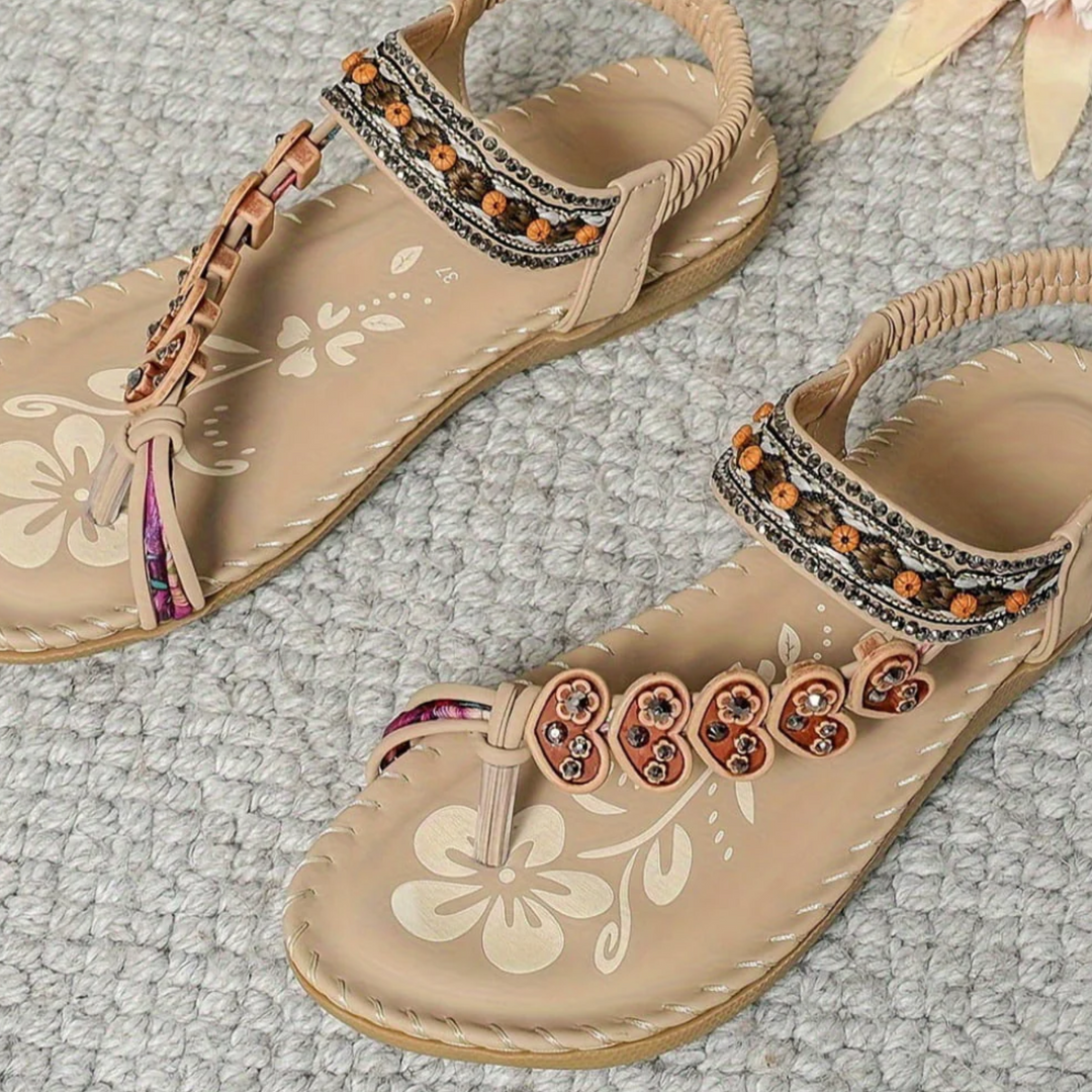 Beige sandals with floral designs and decorative straps on a textured surface